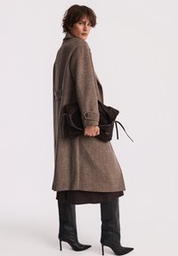 Brązowy płaszcz z włókna wełnianego o prostym kroju, w połączeniu z ciemnobrązową skórzaną kopertówką i czarnymi wysokimi botkami na szpilkach.