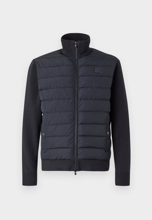 Chaqueta de plumas en color navy con cierre delantero de cremallera, parte superior acolchada texturizada, mangas y dobladillo de punto sólido, y cuello alto. Incluye botones a presión.