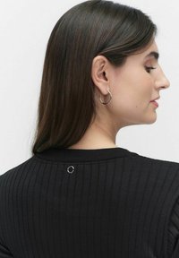 Sort ribbet sweater vist fra siden, med en rund accent detalje på den bageste halsudskæring og en model iført sølvfarvede hoops.