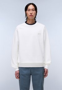 Hvit sweatshirt med rund hals, ribbestrikkede mansjetter og hem. Har en lys grå logo på brystet. Brukes med blå cargo-bukser.