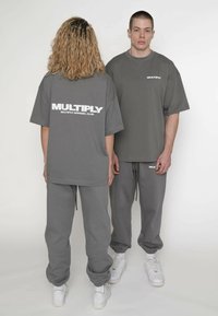 Graue, übergroße T-Shirts und passende Jogginghosen aus weichem Stoff. Auf der Rückseite prangt ein großes weißes Logo: "MULTIPLY APPAREL CLUB." Weiße Sneakers.