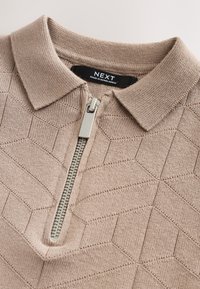 Tricou polo maro deschis cu fermoar, având un model geometric texturat, guler scurt și fermoar argintiu. Eticheta brandului este vizibilă în interiorul gulerului.