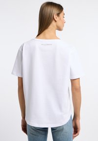 Witte katoenen t-shirt met een ronde hals en korte mouwen. Heeft een klein logo gedrukt op de achterkant nabij de halslijn.