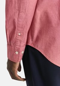 Lange mouwen, roze shirt van een gestructureerde stof, met twee met knopen sluitende manchetten en een gebogen zoom. De kraag is casual en de pasvorm is ontspannen.