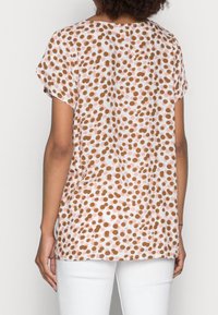 Top a maniche corte in tessuto leggero con sfondo rosa e pois marroni e bianchi. Vestibilità ampia con scollatura rotonda e spacchi laterali.