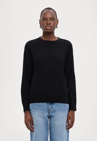 Maglione nero lavorato a maglia con scollo rotondo e maniche lunghe. Orlo e polsini a costine; design minimalista con un logo discreto sul petto.
