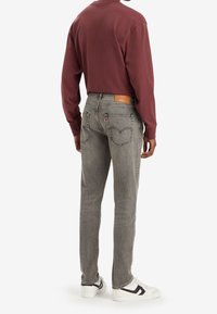 Grå denimjeans med rak passform, tillsammans med en vinröd långärmad tröja och vita sneakers, med en skinnlapp baktill.