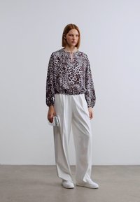 Μπλούζα με λεοπάρ σχέδιο, άνετη εφαρμογή και μανσέτες με σούρες, συνδυασμένη με ψηλόμεσο λευκό παντελόνι και λευκά αθλητικά παπούτσια. Περιλαμβάνεται ασημένια τσάντα χειρός.