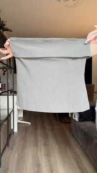 Top in lino grigio con scollatura larga e arrotolata, forma piatta e lati dritti. Il tessuto teso mostra una texture liscia e cuciture minime.