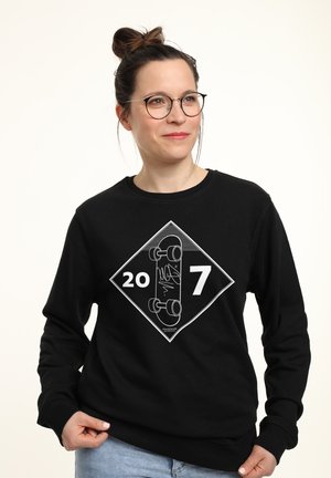 Felpa nera con un grafico bianco a forma di diamante che presenta un design di skateboard e il testo "207". Tessuto morbido, colletto rotondo e maniche lunghe.