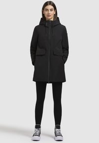 Black hooded parka with a front zipper, two front pockets, and cinched waist. Paired with black leggings and sneakers with white accents.