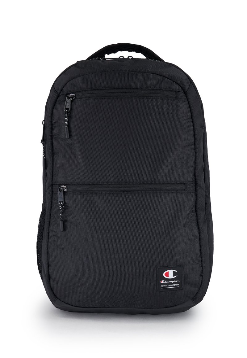 Zaino nero realizzato in tessuto testurizzato. Presenta due tasche anteriori con zip e una maniglia superiore. Include un patch con logo nella parte inferiore anteriore.