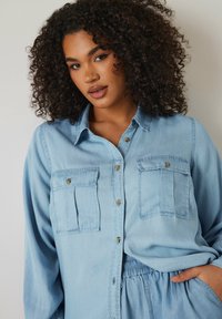 Camicia di jeans azzurro chiaro con davanti a bottoni, due tasche sul petto con pattina e maniche lunghe, realizzata in un tessuto morbido e testurizzato.