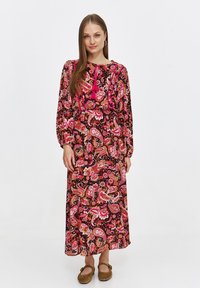 Maxi dress with long sleeves, black background, and pink paisley pattern. Features a cinched waist and tassel detail at the neckline.