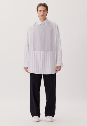 Gestreepte button-up shirt in wit en lichtblauw, met een losse pasvorm, lange mouwen en een borstzak, gecombineerd met zwarte broek en witte schoenen.