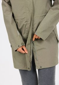 Olijfgroene waterdichte jas met een rits aan de voorkant en drukknopen, voorzien van een gladde textuur en een verstelbare zoom voor een goede pasvorm.