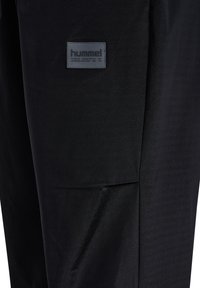 Zwarte sportieve broek met een soepele textuur, met een logopatch aan de zijkant. De stof is licht en gestructureerd voor optimale prestaties.