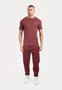 Bordowa krótka koszulka z okrągłym dekoltem, zestawiona z pasującymi bordowymi dresami. Oba wykonane są z gładkiego, rozciągliwego materiału.