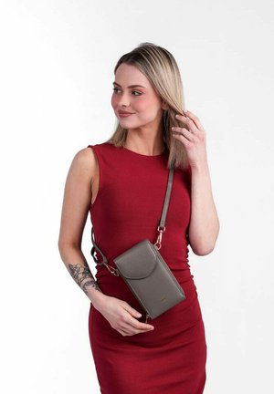 Šedá crossbody taška se zavíráním na klopu, vyrobená z hladkého materiálu. Má dlouhý popruh a nenápadný detail loga na přední straně.