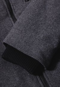 Giacca grigia lavorata a maglia con zoom sulla manica, che presenta un motivo testurizzato, polsino a coste nero e dettaglio con cerniera. Materiale morbido e spesso.