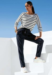 Gestreepte lange mouwen top in wit en marineblauw, gecombineerd met marineblauwe joggingsbroeken. Witte sneakers. Soepele textuur, ontspannen pasvorm. Minimale accessoires.