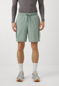 Šviesiai žali krovinių šortai su elastinga juosmens juosta ir raišteliu, turi šonines kišenes ir lygų, lengvą audinį.