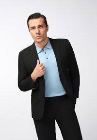 Schwarze Anzugjacke über einem hellblauen Polohemd mit Kragen und drei Knöpfen. Glatter Stoff mit taillierter Passform, keine sichtbaren Muster.