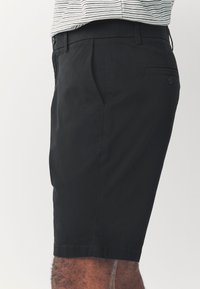 Zwarte korte broek van lichtgewicht stof, met een vlakke voorkant, steekzakken aan de zijkant en een enkele achterzak met een knoopdetail.