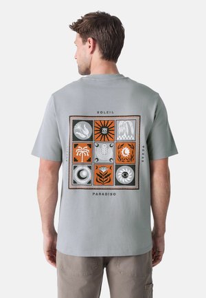 Grå kortærmet t-shirt med et multicoloreret grafikprint på ryggen, bestående af forskellige designs i orange, sort og hvid.