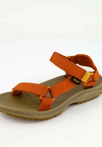 Sandalias naranjas con correas, suela de goma texturizada, correas de nylon ajustables y base marrón. Presenta detalles amarillos y etiqueta de la marca.
