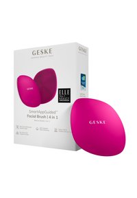 Brosse facial en silicone rose avec surface texturée et forme ergonomique. Présentée dans une boîte blanche avec branding et détails du produit.