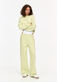 Hellgrüner Pullover und passende, weit geschnittene Hose aus einem weichen, glatten Stoff. Die Hose hat einen elastischen Bund und seitliche Taschen.