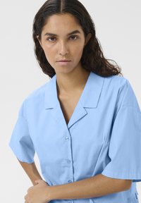 Camicia azzurro chiaro a maniche corte con colletto, chiusura a bottoni e tessuto liscio, caratterizzata da una vestibilità rilassata e semplicità.