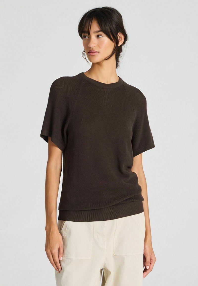 Maglione a maniche corte di colore marrone scuro, in maglia, con scollatura rotonda e texture a coste, abbinato a pantaloni cargo di colore chiaro. Design semplice e rilassato.