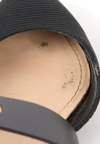 Gros plan d’une semelle intérieure de sandale en cuir beige usée avec un tissu noir et une sangle noire avec un rivet en laiton.