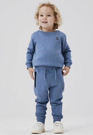 Felpa azzurra con scollo rotondo e piccolo logo nero, abbinata a pantaloni jogger coordinati con tasche laterali e polsini elastici.