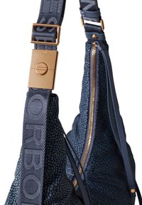 Blaue Stoff-Schultertasche mit strukturiertem Muster, goldfarbenen Beschlägen und einem gemusterten Trageriemen mit Logodetail. Sichtbarer Reißverschluss.