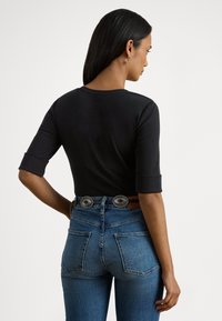 Top preto de três quartos de manga combinado com jeans de ganga azul de cintura alta, apresentando um cinto castanho com fivelas circulares prateadas.