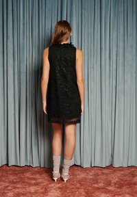 Μαύρο φόρεμα από δαντέλα με αμάνικο σχέδιο, υφασμάτινο λουλουδάτο μοτίβο και διάφανο τελείωμα. Συνδυασμένο με ανοιχτό γκρι κάλτσες μέχρι το γόνατο και διάφανα τακούνια.