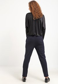 Black, lightweight top with relaxed fit, paired with navy, tailored trousers featuring side pockets and a smooth texture, visible cuff detail.