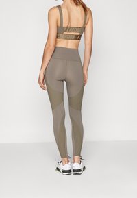 Reggiseno sportivo verde oliva con logo stampato sulla fascia, abbinato a leggings a vita alta coordinati con pannelli testurizzati e cuciture.