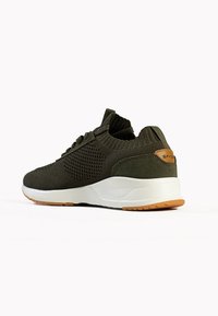 Sportliche Schuhe mit olivgrünem Mesh-Obermaterial, Gummisohle und weißem Zwischensohleneinsatz. Mit strukturierten Akzenten und einfachem Schnürsystem.