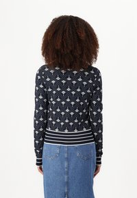 Navy patterned sweater with white floral design, long sleeves, and ribbed striped hem. Worn with a light blue denim skirt.