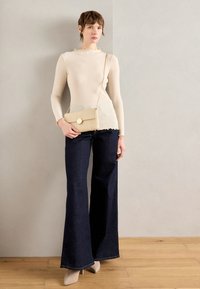 Beige ribbed top s dlouhým rukávem se vroubkovaným výstřihem, kombinovaný s tmavě modrými širokými kalhotami a světle béžovou krosnou s kulatým zapínáním.