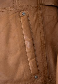 Braunes Ledermaterial weist eine glatte Textur, gestickte Details und eine rechteckige Tasche mit einem metallenen Druckknopfverschluss an der Seite auf.