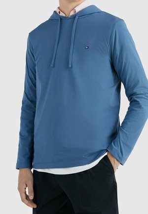 Maglione blu a maniche lunghe con cappuccio in tessuto morbido, caratterizzato da un piccolo logo sul petto, aperture laterali e lacci regolabili sul cappuccio.
