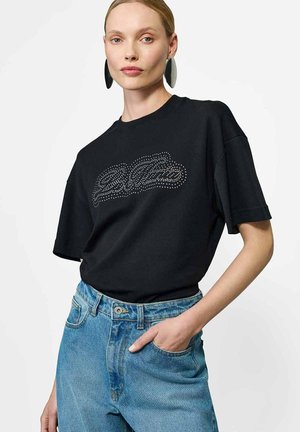 Czarny t-shirt z krótkim rękawem z kropek na przedzie, w połączeniu z jasnoniebieskimi spodniami z wysokim stanem.