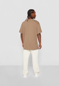 Tricou din bumbac, cu maneci scurte si croiala lejera, de culoare maro deschis. Asortat cu pantaloni albi si tenisi. Design simplu si casual.