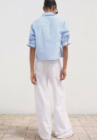Blau-weiße gestreifte kurze Bluse mit hochgeschlagenen Ärmeln, kombiniert mit lockeren weißen Hosen. Glatte Stoffstruktur, minimalistische Details.