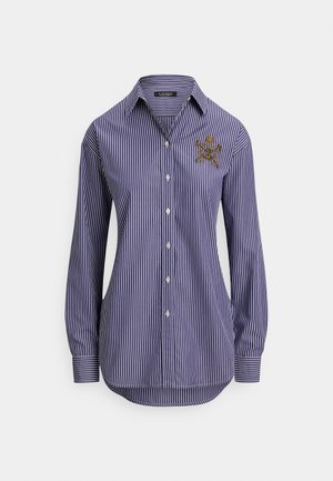 Niebiesko-biała koszula w paski z długim rękawem, kołnierzykiem na guziki oraz haftowanym detalem na lewej piersi. Posiada zaokrąglony dół.